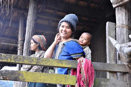 to kvinner, en av dem med en baby på armen, smiler mot kamera utenfor en hus i landsbyen Hlo Lang Pan i Myanmar.